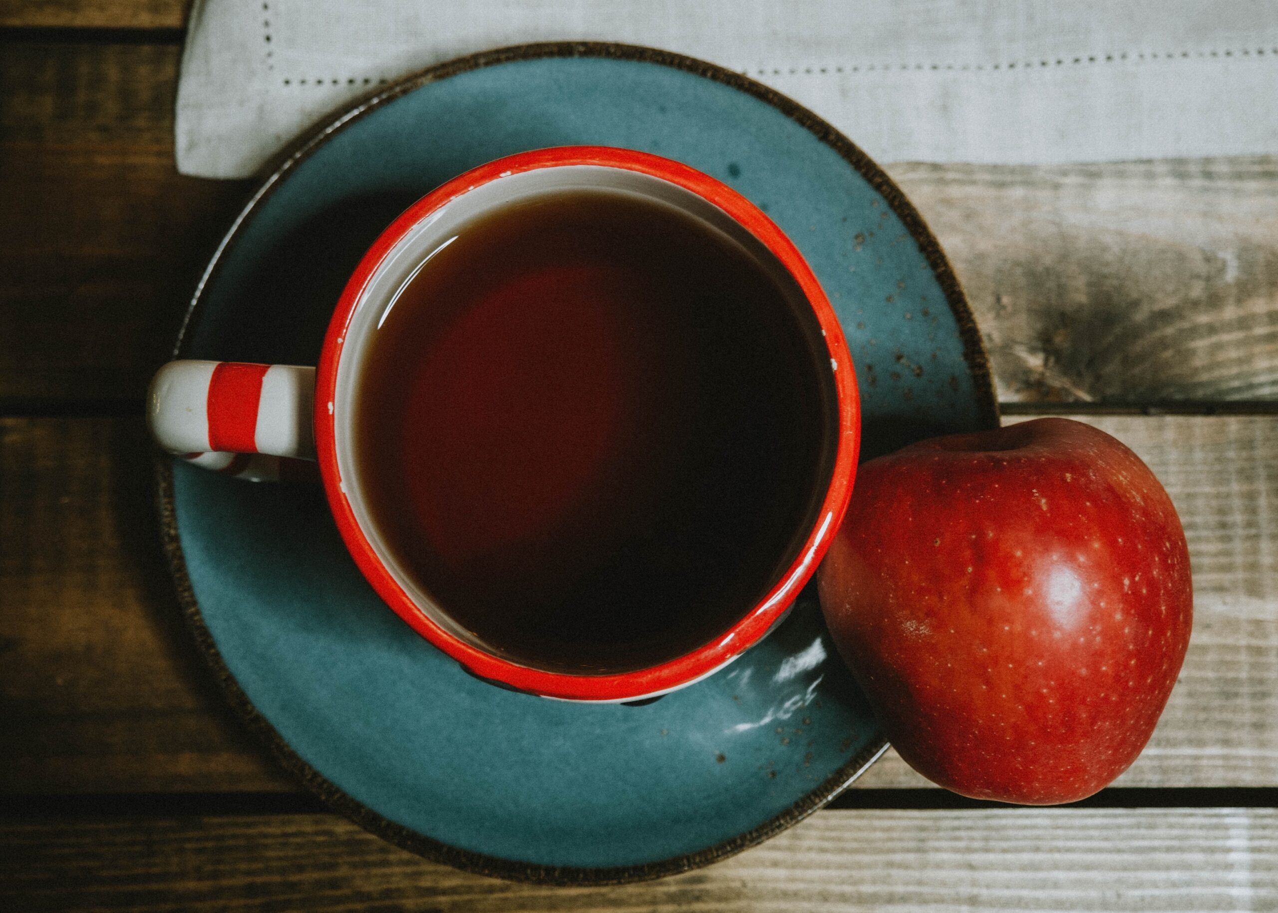 Blå keramikkopp med te och ett rött äpple på bord, sett uppifrån
